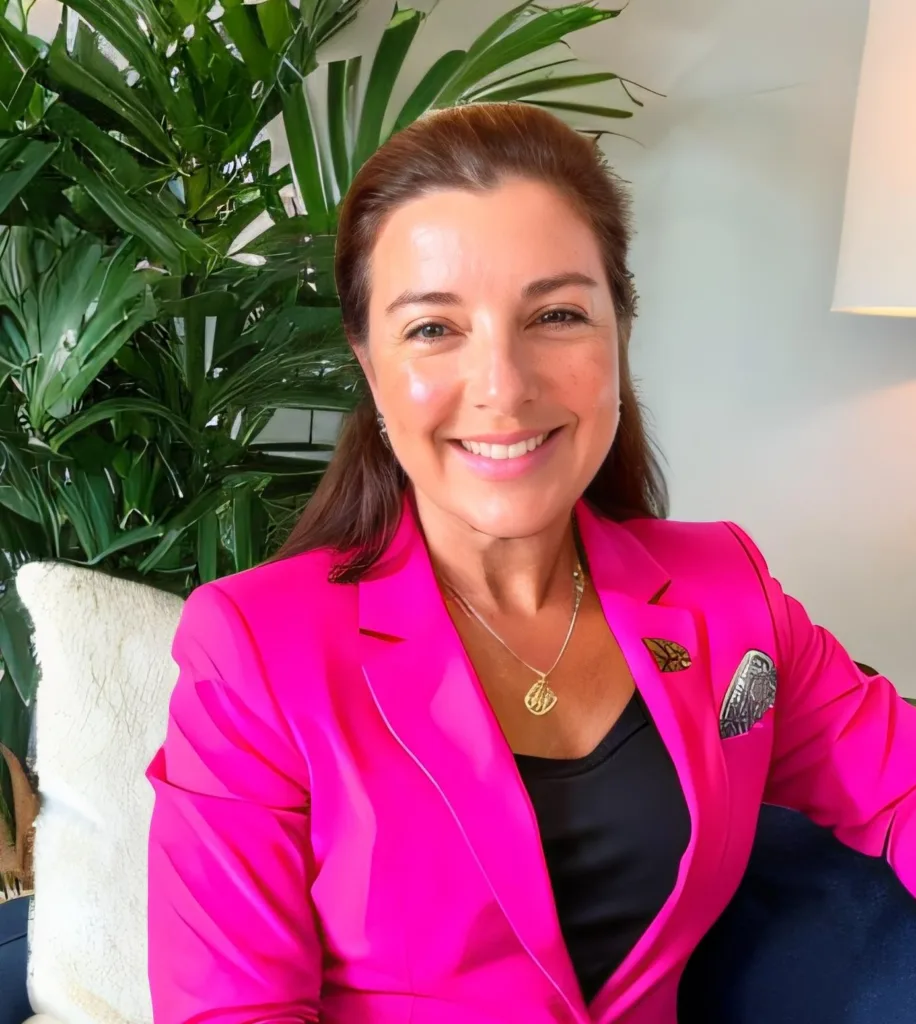 A woman wearing a pink suit and sitting in front of a plant