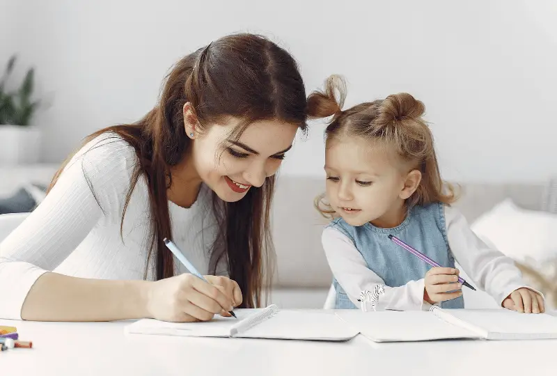 rota nanny is smiling and doing homework with a small child.