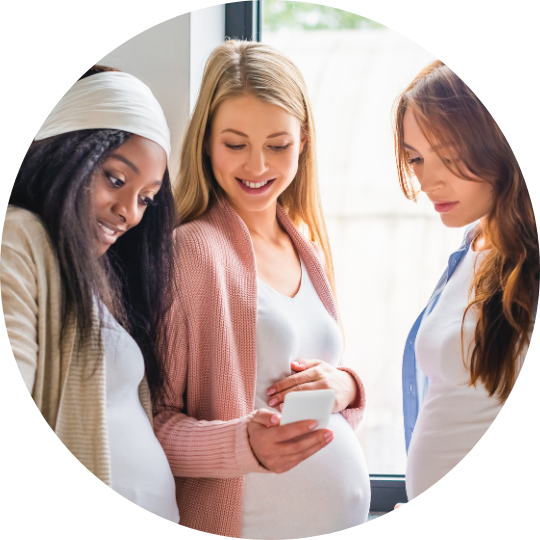 3 pregnant women talking. 1 woman is showing the Kensington Nanny website on her phone. Giving Kensington Nanny a great nanny agency review.