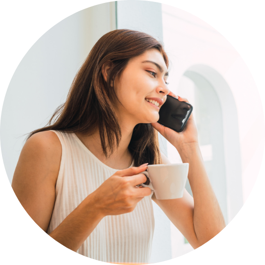 woman talking on the phone and holding her morning cup of tea. She is talking to a friend and giving Kensington Nanny a great nanny agency review.