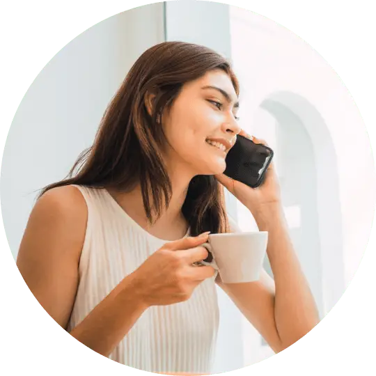woman talking on the phone and holding her morning cup of tea. She is talking to a friend and giving Kensington Nanny a great nanny agency review.