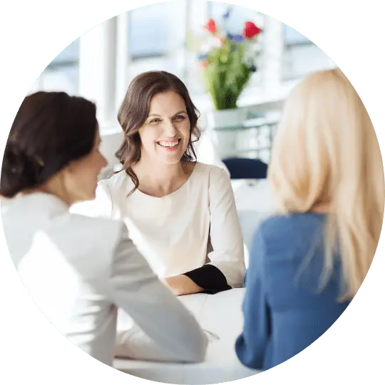 3 women sitting at a table talking. One woman is giving Kensington Nanny a great nanny agency review.