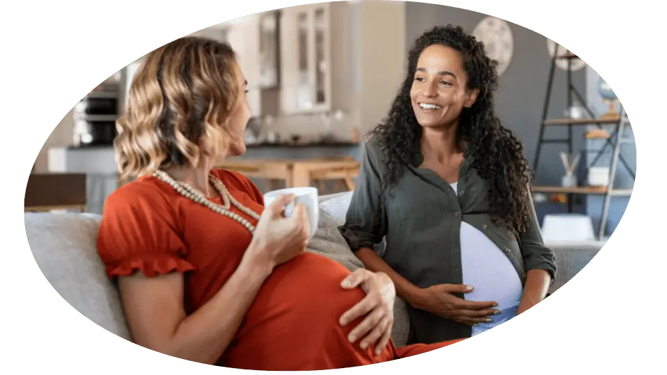 2 pregnant women sitting on the couch having tea. Giving Kensington Nanny a great nanny agency review.
