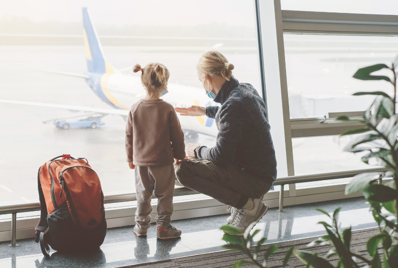 Image shows a travel nanny with a small child at an airport. The travel nanny is pointing to the plane and engaging with the child.
